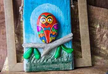 Crafts made of stone, paints and wood. Owl on a branch.