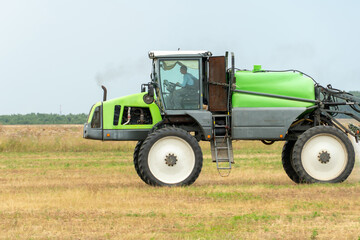 Fototapeta premium self-propelled sprayer works on a field on a warm sunny day. Spraying the Crop. Tractor with the help of a sprayer sprays liquid fertilizers in the field.
