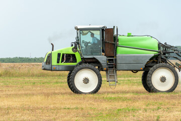 self-propelled sprayer works on a field on a warm sunny day. Spraying the Crop. Tractor with the help of a sprayer sprays liquid fertilizers in the field.