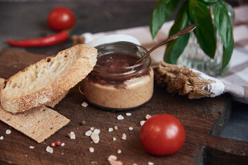 Handmade chicken pate in a glass jar on a wooden board .