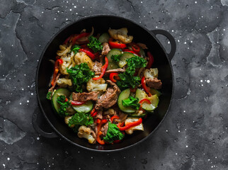 Quick beef stew with zucchini, cauliflower, sweet pepper, kale in a cast-iron pan on a dark background, top view