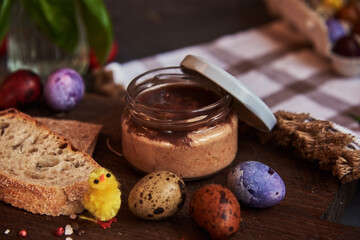 Meat pate in a glass jar on a cutting board and painted quail eggs. Easter background, meat delicacies.