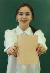 Young beautiful happy girl in the role of a teacher or student near the blackboard with a textbook in her hands.