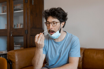 Portrait of concentrated young man taking a Self-swabbing home tests for COVID-19 at home with...
