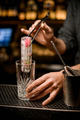 Fototapeta na wymiar barman holds piece of ice with tongs and puts it into crystal glass on bar counter