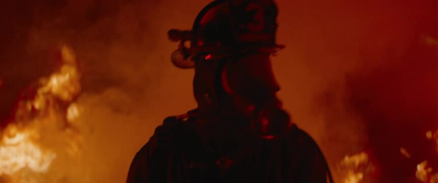 HANDHELD TRACKING Dramatic shot of American firefighter in full gear walking through smoke and fire. Shot with 2x anamorphic lens