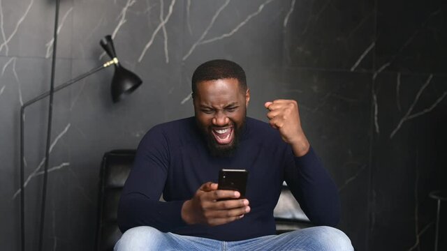 Goal achievement. Overjoyed African-American businessman looks at the smartphone screen and rejoices, happy with unexpected opportunity black guy scream yes, received promotion, won in video game