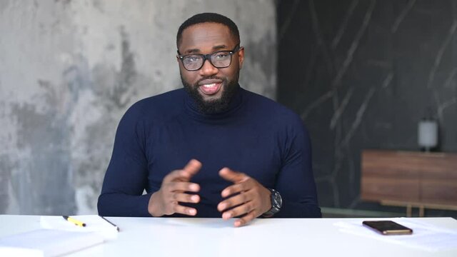 Video conference with a smart and smiling African-American male entrepreneur, virtual meeting with dark skinned employee. Webcam view of black guy waving hello in the camera, greeting interlocutor