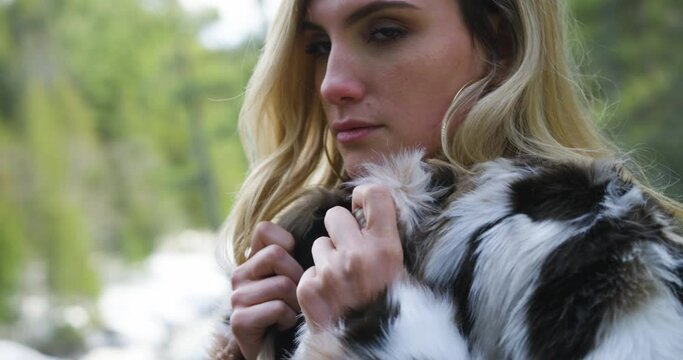 Confident young woman wearing a fur jacket poses for the camera in a winter forest setting. Close up shot.