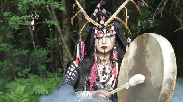 Shaman plays the drum and moves closer, fills the frame with face. Smoke, slow motion. Part 2 of 2.