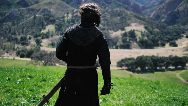 Man in medieval outfit walks.  Shot from behind with steady camera tracking in.  mountains in background. slow motion 60fps