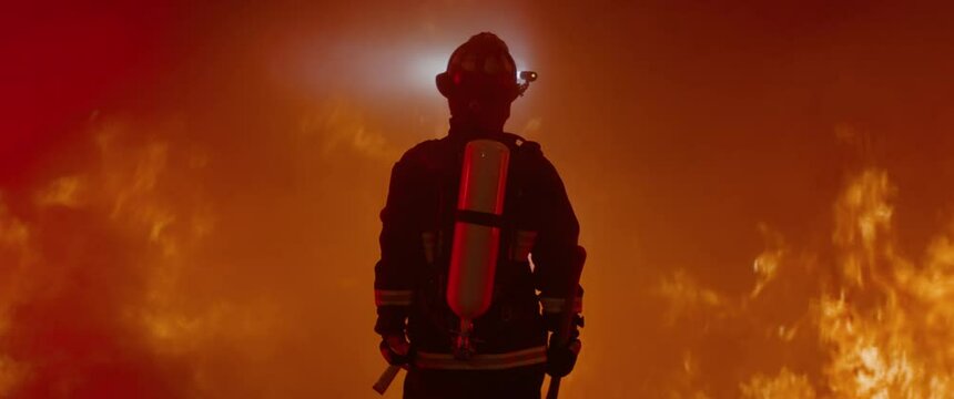 Dramatic silhouette of American firefighter in full gear exploring the huge fire zone. Shot with 2x anamorphic lens 