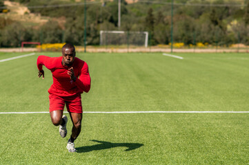 Obraz premium Professional black afro runner running fast in a field with serious concentrated face.