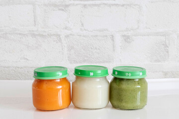 Glass jars for children with mashed potatoes for feeding children up to a year. Introduction of vegetables into the child's diet. Broccoli, carrots, cauliflower. Light background.