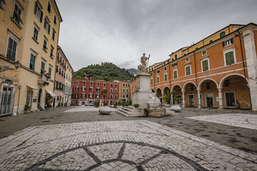 Fototapeta na wymiar Cityscape. Carrara city center: Piazza Alberica with the commemorative monument in the center and the Ducal Palace , and small open doors cafes, shops in Tuscany, Italy