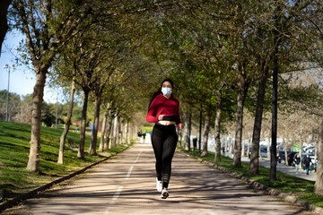 Young woman with face mask because covid, running in the park. Active person outdoors.