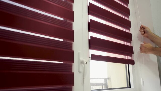 Close up shot of a male's hand opening striped blinds on a window. Modern fabric roller blind. Focus on the hand