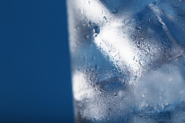 Ice cubes in a glass with crystal clear water on a blue background.