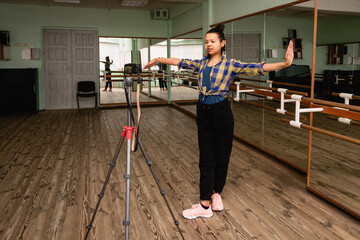 Young woman vlogger records dance on camera on tripod in choreographic hall. 