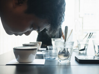Professional barista testing the smell of a new coffee,Close up view portrait of a beautiful young man professional Q Grader test and inspecting the quality of coffee from cup on the table.