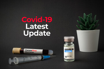 COVID-19 LATEST UPDATE text with a bottle of vaccine, blood sample vacuum tube and syringe on black background. Covid-19 or Coronavirus Concept.