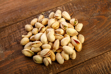 Pistachio nuts are sprinkled on a dark wooden table.