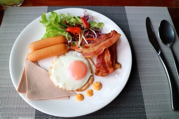 American breakfast set with fried egg, ham, sausage, bacon, and salad on white plate. Food concept.