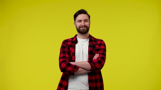Portrait of a handsome young man with a beard in the studio on a yellow background. The man stands with his arms crossed in front of him and smiles mysteriously. Close up. Slow motion ready 59.97fps.
