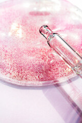 Drop of pink transparent facial serum with pipette . Skincare Liquid scrub gel macro swatch texture