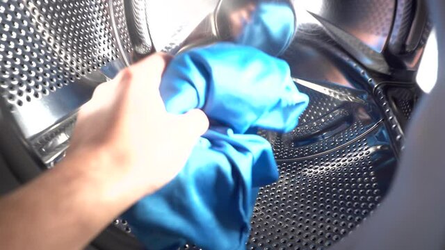 Boy takes out blue clothes from inside the drum of the washing machine. Subjective camera of action. Home cleaning tasks. 