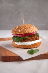 Vegan burger made with red beans, red pepper, spinach and white yoghurt. Fresh delicious vegetarian burger on a cutting board.