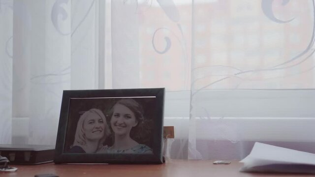 on the desktop there is a frame with a photo, which shows two girls. The table is a mess, with a window in the background.