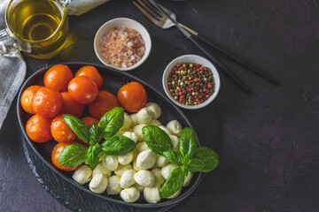 Obraz na płótnie Canvas Mozzarella cheese, basil and tomato cherry in oval black plate, copy space. Ingredients for Caprese salad