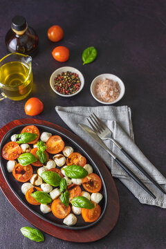 Caprese salad with cherry tomatoes, mozzarella and basil in oval black plate