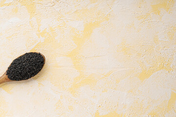 Black sesame on wooden spoon on yellow cement background