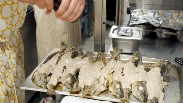Close-up of male chef hands seasoning fried pollock fish with spices in the kitchen.