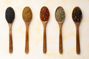 Collection of five spices on wooden spoons on yellow cement background