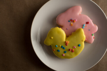 Traditional holiday Easter sugar cookies frosted in spring colors on a plate. Cookies are in rabbit and duck shapes with yellow duck in the foreground.