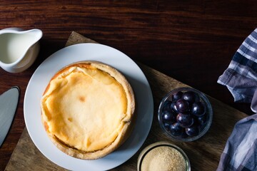 Grandma's homemade cheesecake besides grapes and milk and sugar on dark wooden board