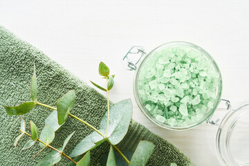 Green towels, bath salt and eucalyptus branch on white wooden background, SPA concept