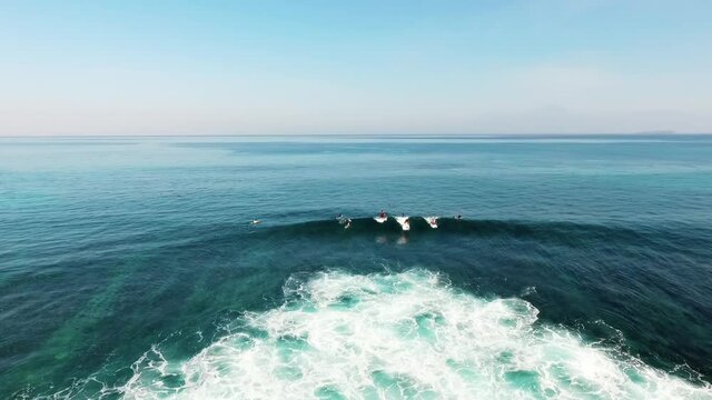 Aerial drone view following surfers, catching a wave, in clear waters of Indonesia