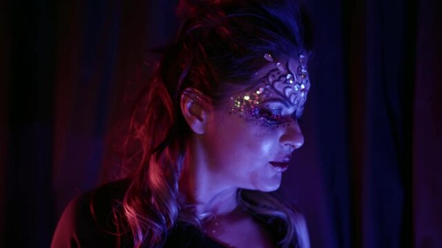 sexy woman is dancing in darkness, bright makeup on her face and shiny crystals