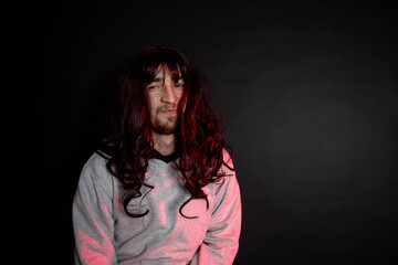 Portrait of young transgender woman on black background. Funny bearder man wearing wig.