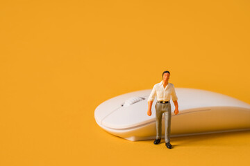 Miniature people on a yellow background, a male programmer or businessman near a computer mouse