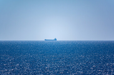 Calm blue sea with the silhouette of a large ship on the horizon