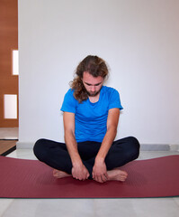 A Spanish young bearded male in sportswear practicing yoga on the yoga mat at home