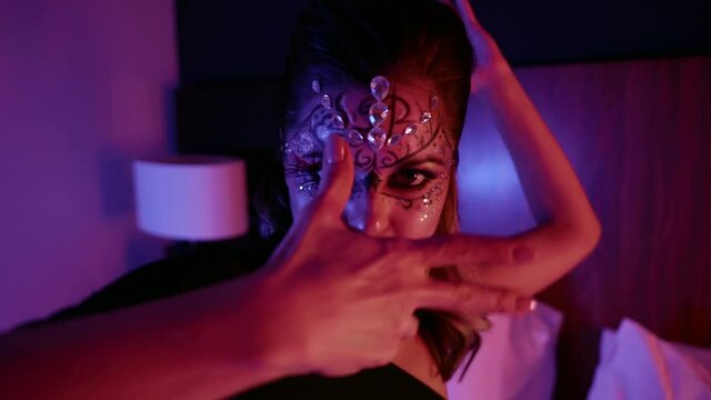 enigmatic lady with scenic makeup with crystals is dancing on bed in bedroom, flirting with camera