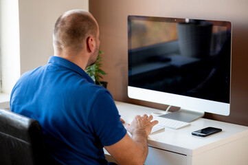 Fototapeta premium Back view of businessman using computer while sitting at desk in home office