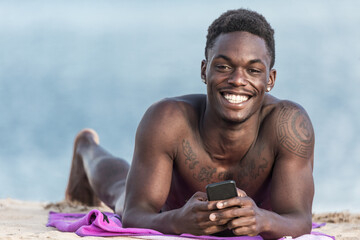 Cheerful black man with smartphone on beach