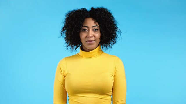 African woman with curly hair looking to camera, smiling. Beautiful model girl in yellow wear on blue studio background.